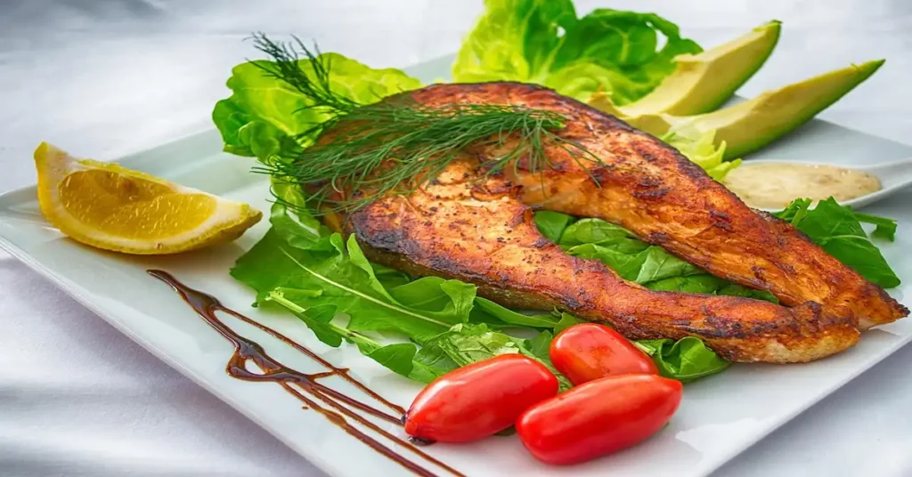 A dish with a piece of fish, crisp lettuce, and ripe tomatoes, paired with a glass of wine, highlighting foods for clear skin.